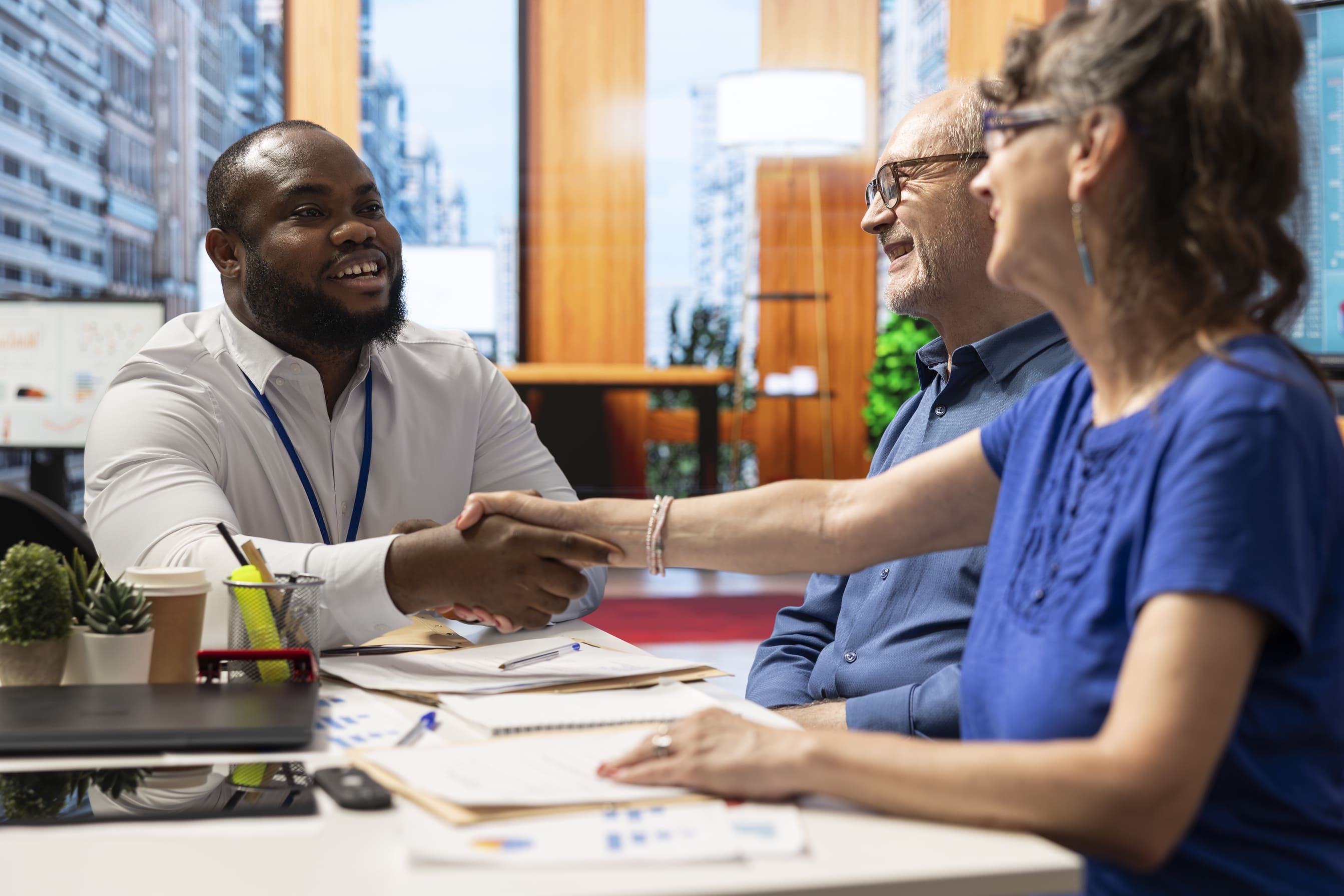 A man shaking hands with a couple at a desk